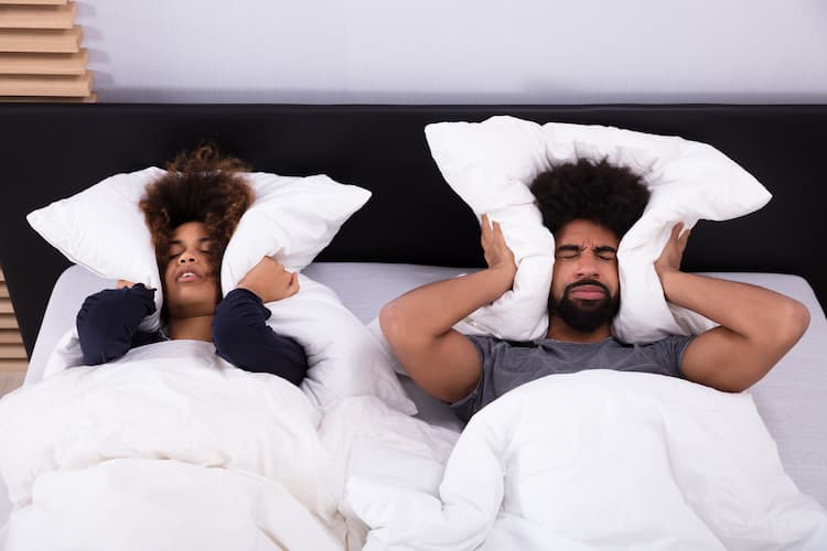 Young couple covering their ears with pillows.